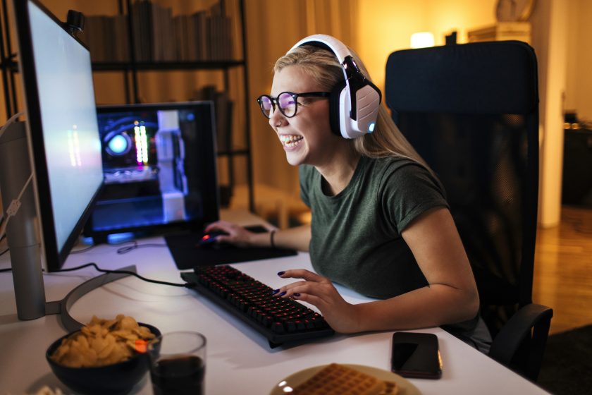 © iStock / mihailomilovanovic Junge Frau mit Brille lachend beim Gamen vor dem Bildschirm