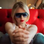 Blonde Frau auf rotem Sofa mit sportlicher Sonnenbrille