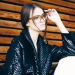 Frau mit Lederjacke und Brille sitzt am Boden