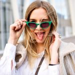 Junge Frau mit grüner Sonnenbrille streckt Zunge heraus