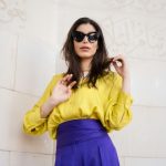 Frau mit gelber Bluse, lila Rock und schwarzer Sonnenbrille