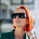 Frau mit hellroten Haaren, schwarzer Sonnenbrille und grünem Blazer