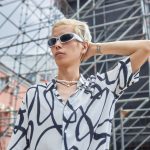 Junger blonder Mann mit sportlicher Sonnenbrille und gemustertem Hemd in urbanem Setting