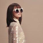 Junge, dunkelhaarige Frau mit großer Sonnenbrille und glänzender Bluse