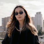 Dunkelhaarige Frau mit Sonnenbrille mit einer Stadt als Hintergrund