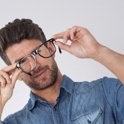 Mann hält prüfend seine Brille vor sich