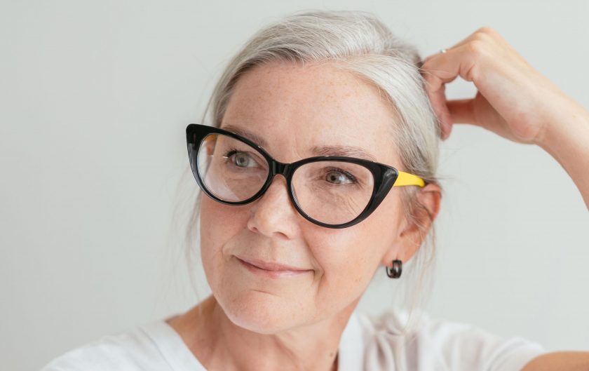 Frau mit grauen Haaren und schwarz-gelber Brille